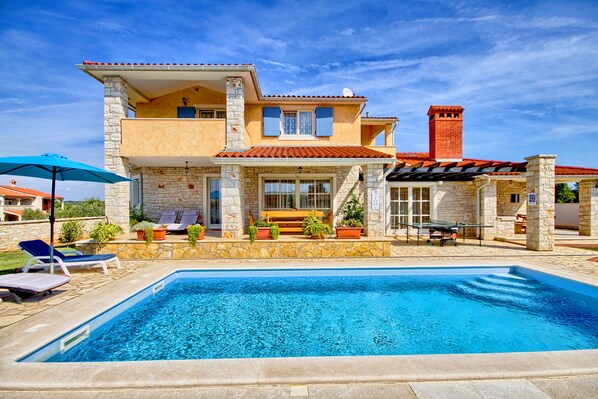 A two-story house with a swimming pool, stone facade, and a red-tiled roof.