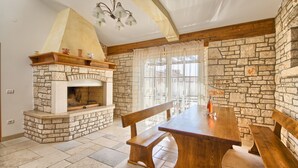 Une cheminée en pierre avec une cheminée en bois, une table à manger en bois avec des bancs et un lustre.