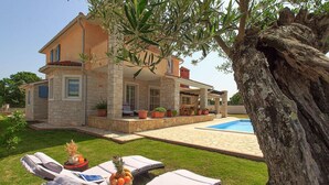 Une maison en pierre à deux étages, dotée d’une piscine, d’un espace salon extérieur et d’un grand arbre.