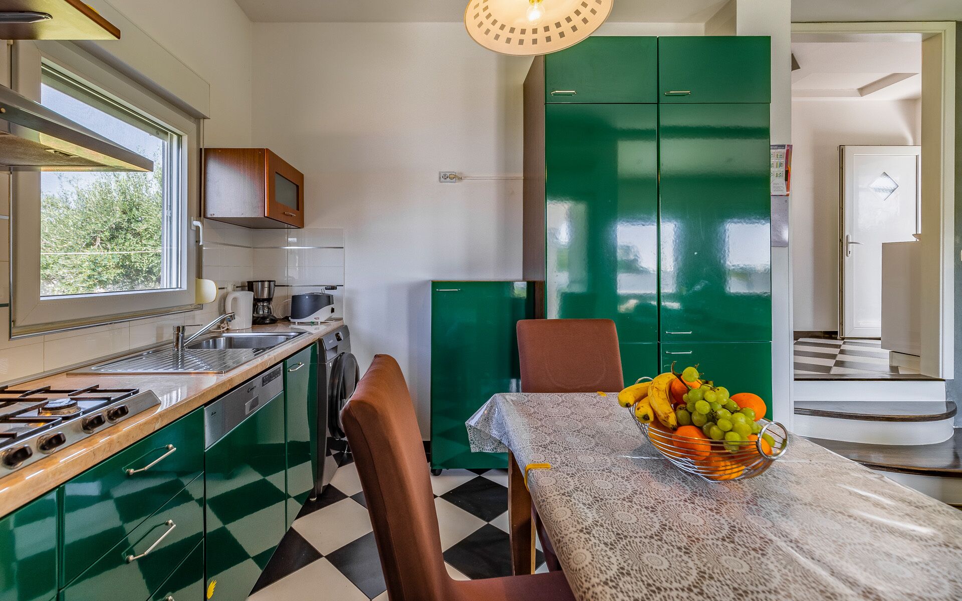 Uma cozinha moderna com armários verdes, um fogão a gás e uma mesa de jantar com uma tigela de frutas.