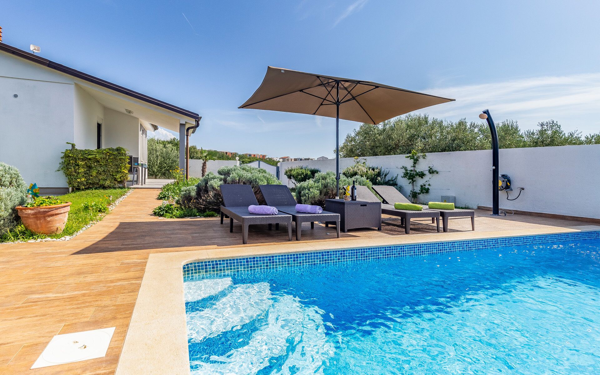 A swimming pool with lounge chairs and an umbrella, surrounded by a wooden deck and potted plants.