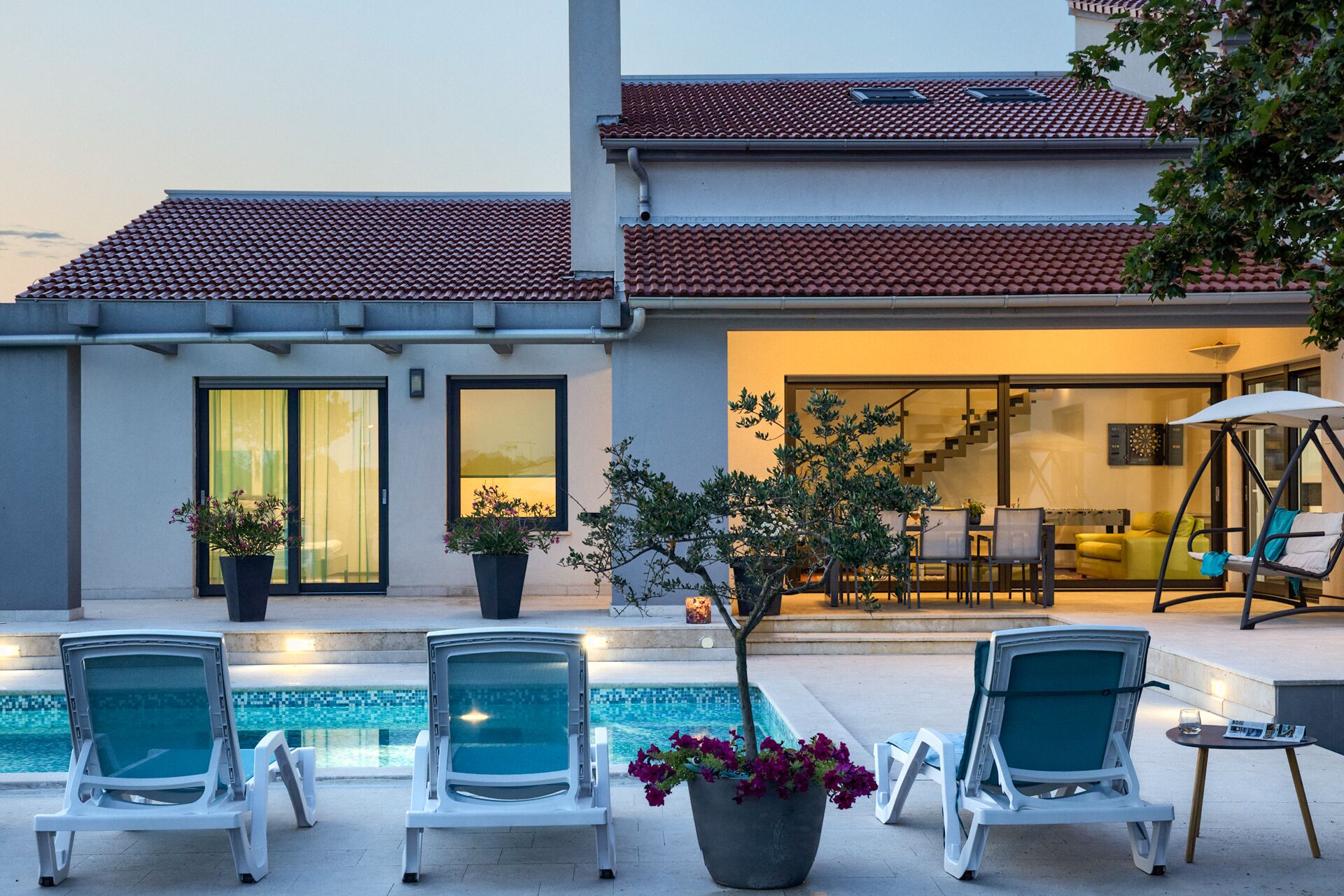 Una casa moderna con piscina, mobiliario exterior y una escalera que conduce al interior.
