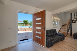 An open door leading to an outdoor area with a pool, a black leather sofa, and a wooden staircase.