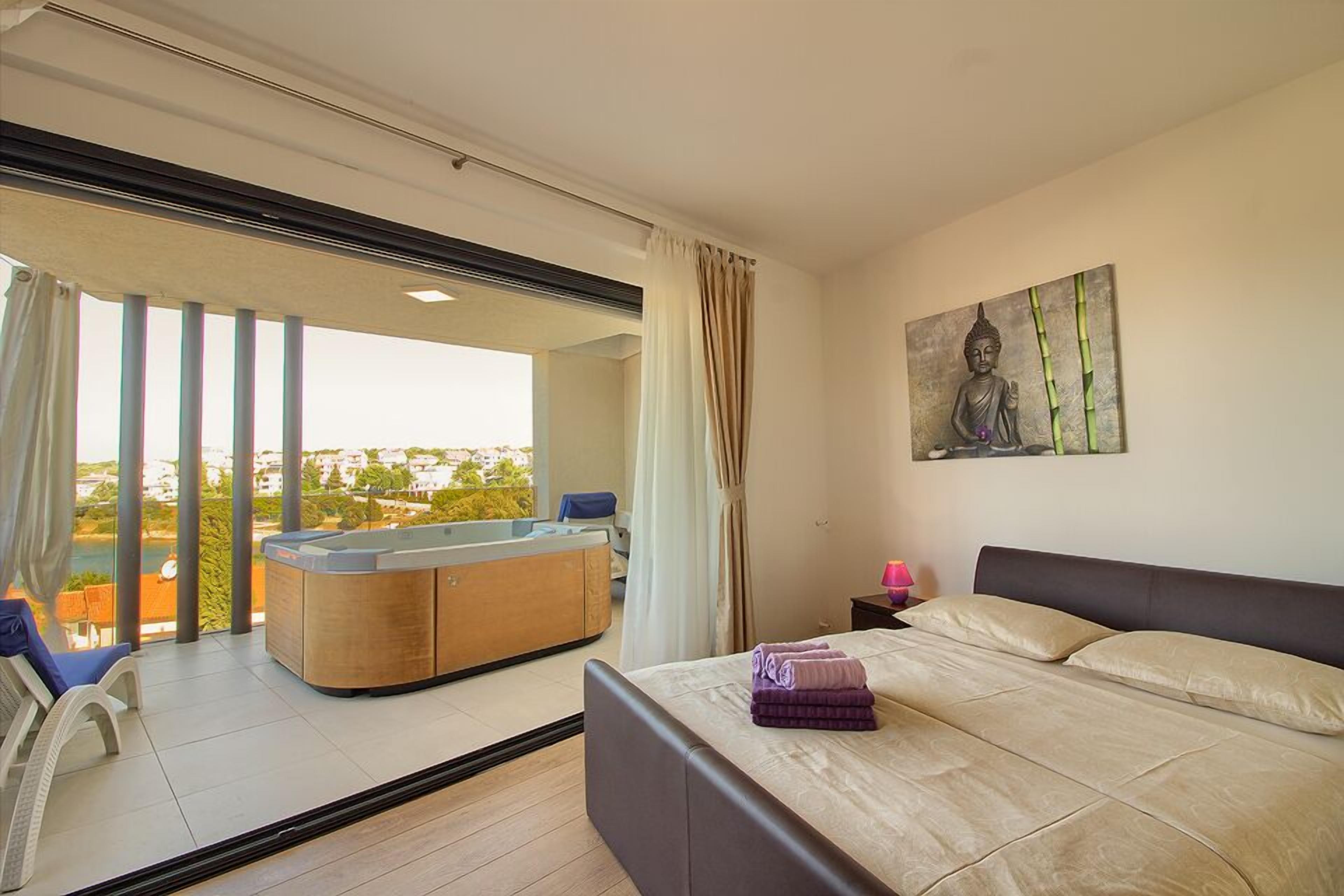 Una habitación de hotel moderna con una cama grande, una silla de masaje, un jacuzzi y vistas a la ciudad.