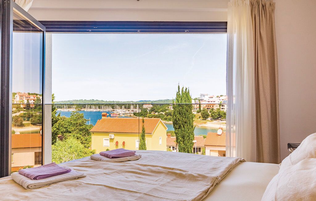 Habitación de hotel con un amplio ventanal que ofrece vistas a un puerto deportivo y edificios.