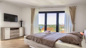 A bedroom with a bed, a TV, a dresser, and a window with curtains.