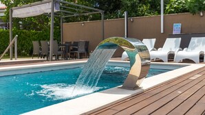 A swimming pool with a modern water feature, lounge chairs, and a covered seating area.