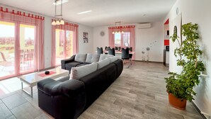 Un salon moderne avec un canapé d’angle noir, une table basse en verre et un coin repas comprenant une table et des chaises. Un pot de plante est placé sur le côté droit.