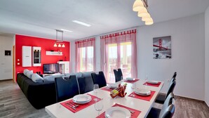 Un coin repas moderne avec une table blanche dressée pour quatre personnes, des sets de table rouges et un rideau à rayures rouges et blanches.