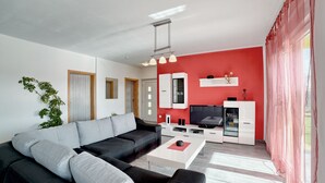 Un salon moderne avec un canapé d’angle noir et gris, une table basse blanche et un mur d’accent rouge.