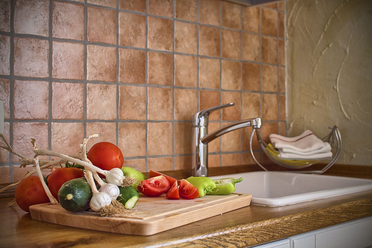 A kitchen counter with a cutting board holding vegetables and a sink with a dish rack.
