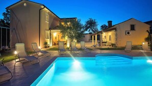 Ein Schwimmbecken mit Liegestühlen und ein Gebäude mit zahlreichen Fenstern und Türen.