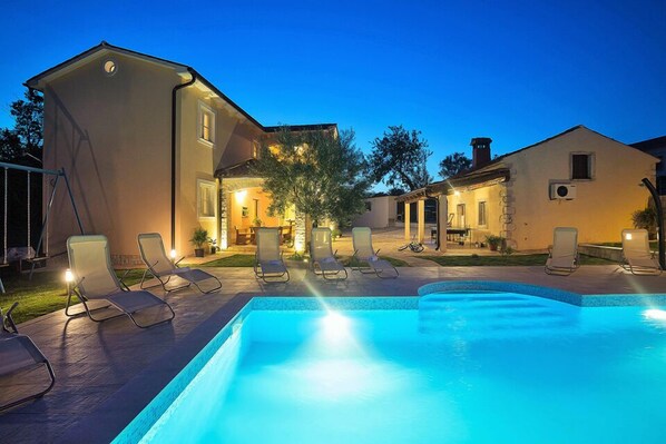 A swimming pool with lounge chairs and a building with multiple windows and doors.