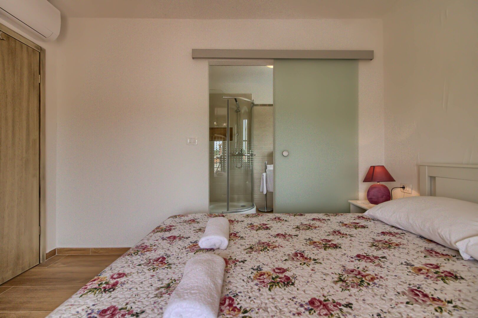 Un dormitorio con cama, mesita de noche, lámpara y baño con ducha.