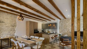 Een moderne keuken met houten balken, een stenen muur, en een eethoek met een houten tafel en witte stoelen.