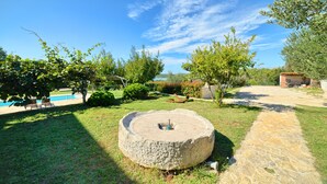 A stone well in a garden with a pool and patio furniture in the background. - Apartment Mare2 (Istria - Banjole) (Banjole)