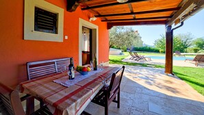 An outdoor dining area with a table set for two, a window with shutters, and a view of a swimming pool and garden. - Apartment Mare2 (Istria - Banjole) (Banjole)