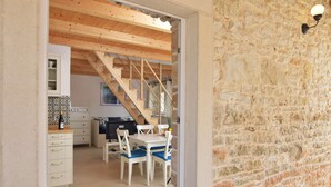 A dining area with a wooden table and chairs, a kitchen in the background, and a stone wall. - Villa Sasso (Istria - Rajki) (Rajki)