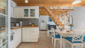 A modern kitchen with white cabinets, a wooden countertop, and a dining area with white chairs and a table. - Villa Sasso (Istria - Rajki) (Rajki)