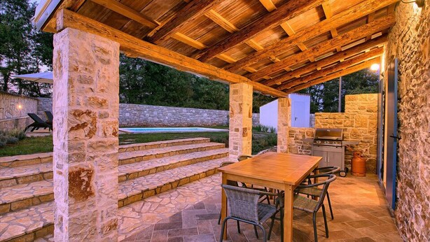An outdoor patio area with stone columns, a wooden pergola, a barbecue grill, and a dining table with chairs. - Villa Sasso (Istria - Rajki) (Rajki)