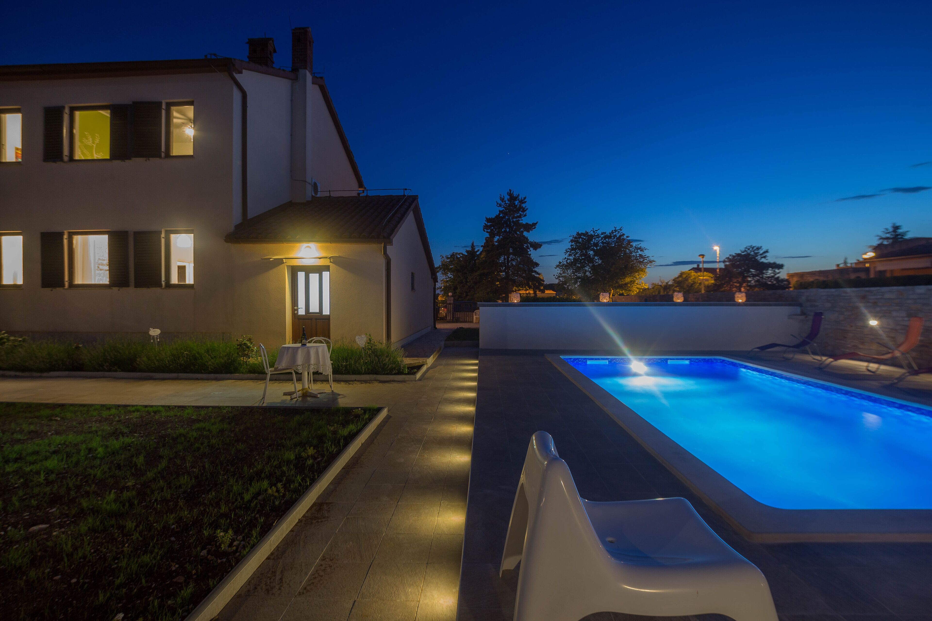 Een modern huis met een zwembad, een goed verlicht pad en een kleine tuin.
