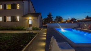 A modern house with a swimming pool, a well-lit pathway, and a small garden area. - Villa Valbandon (Istria - Valbandon) (Valbandon)