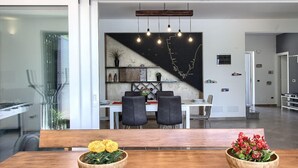 A modern dining area with a wooden table, two wooden bowls of flowers, black chairs, and a wall-mounted light fixture. - Villa Medulin (Istria - Medulin) (Medulin)