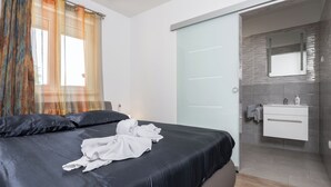 A modern hotel room with a large bed, a bathroom with a mirror and sink, and a sliding door leading to another room. - Villa Eden (Istria - Labin) (Labin)