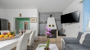 A modern living room with a grey sofa, a dining area with a white table and chairs, a fireplace, and a flat-screen TV mounted on the wall. - Villa Eden (Istria - Labin) (Labin)