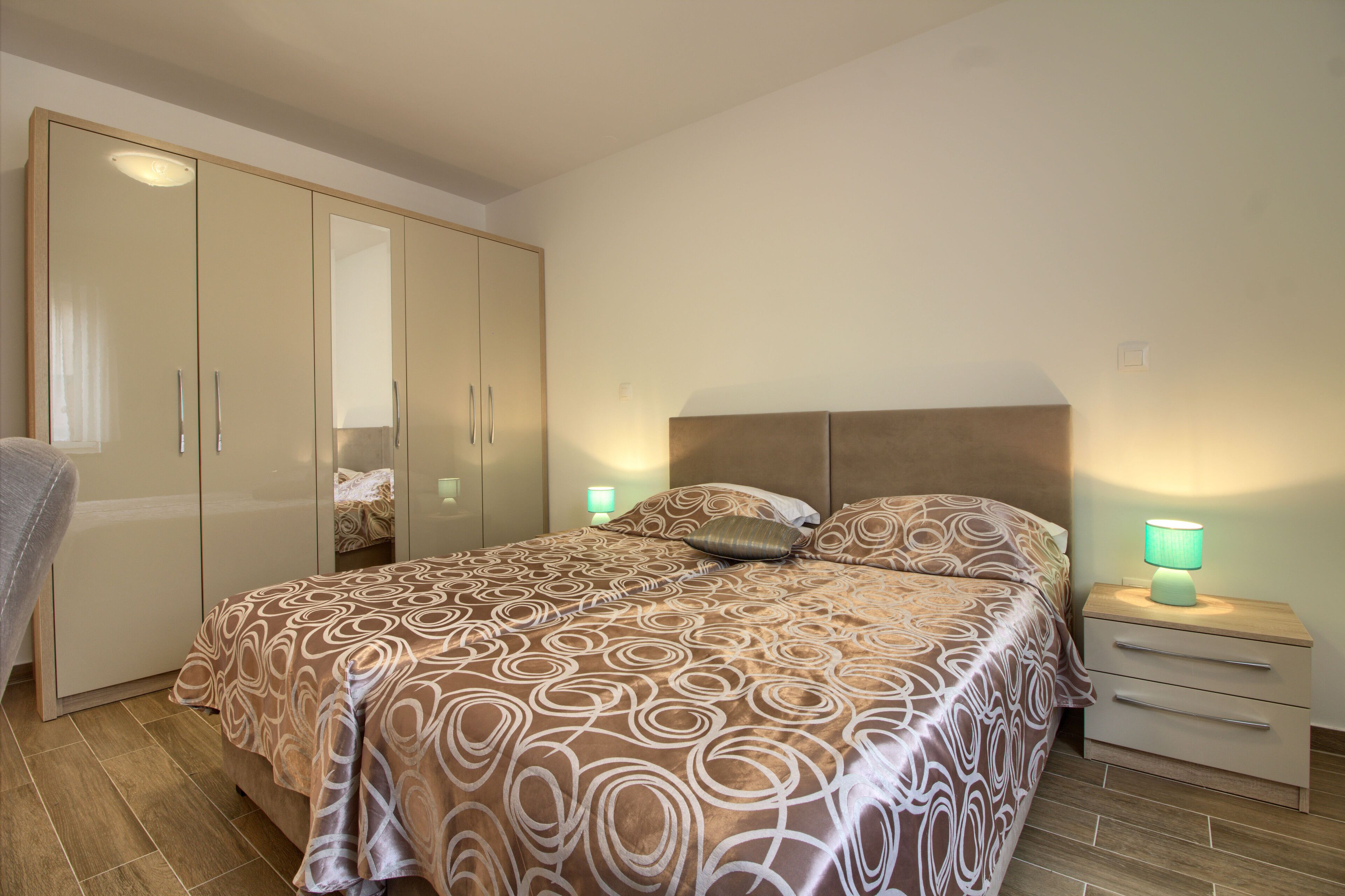 A bedroom with a large bed, a wardrobe, a nightstand, and a lamp.