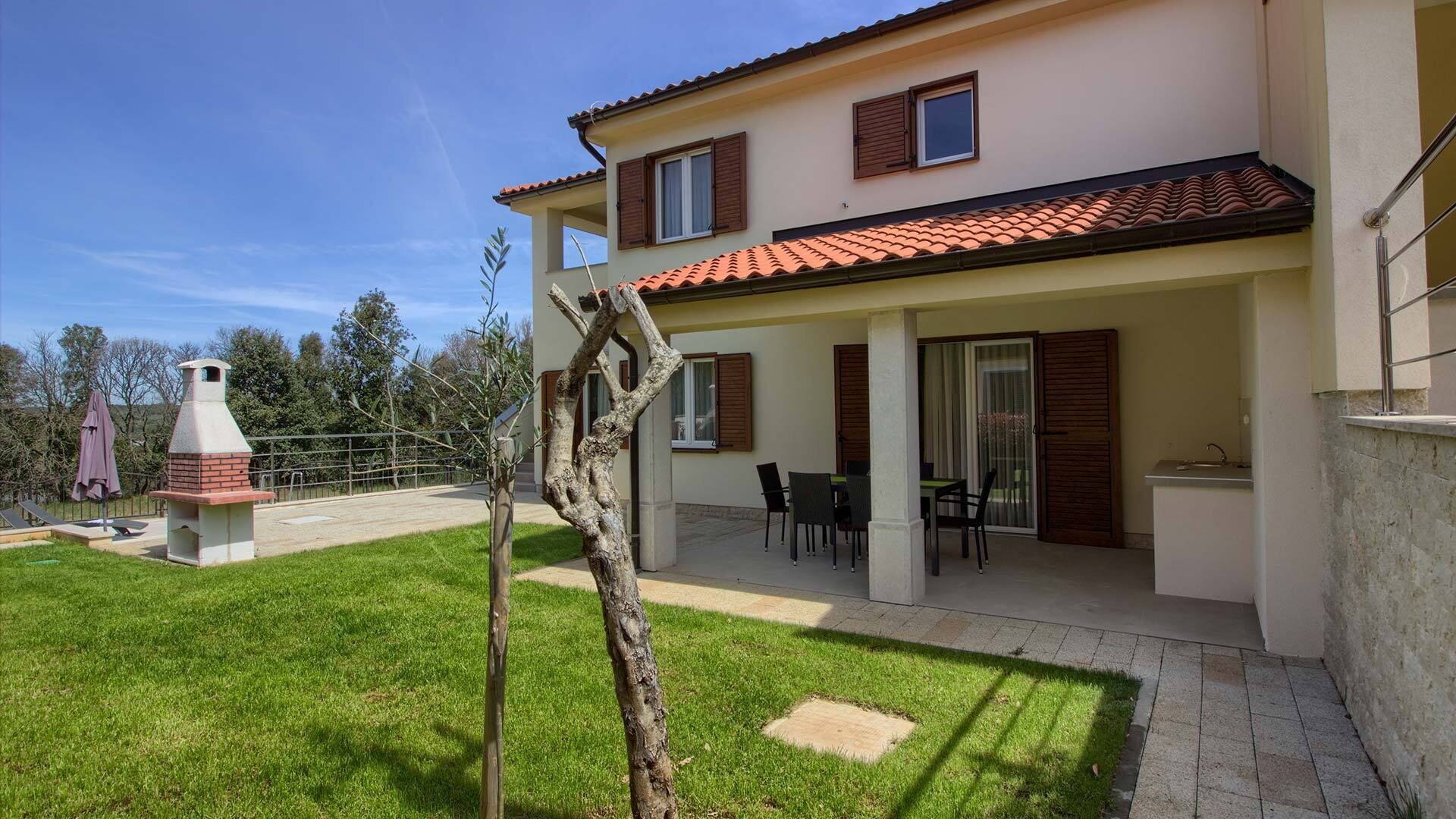 Une maison à deux étages dotée d’un patio, d’un barbecue et d’une table à manger avec des chaises.