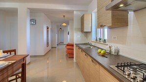 A modern kitchen with wooden cabinets, a gas stove, and a dining area with a table and chairs. - Villa MAREVISTA (Istria - Brovinje) (Brovinje)