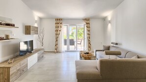 Una sala de estar moderna con un televisor de pantalla plana, armarios de madera, un sofá color beige y un comedor con mesa y sillas.