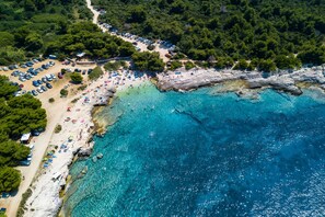 An aerial view of a coastal area with a beach, clear blue waters, and a parking lot with cars. - Villa Manuela (Istria - Banjole) (Banjole)