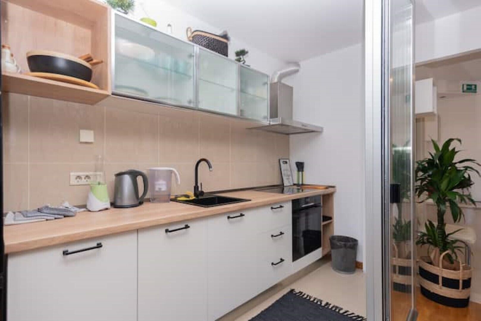 Cozinha compacta com armários brancos, bancada de madeira e painel de vidro.