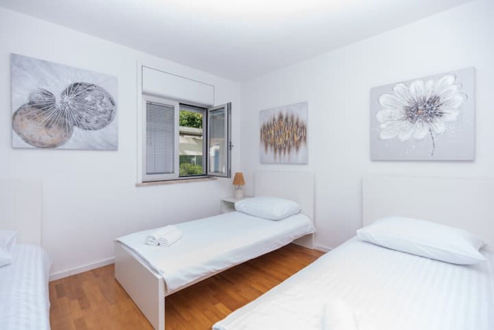 Ein Schlafzimmer mit zwei Einzelbetten, einem Fenster mit Jalousien und zwei an der Wand befestigten Kunstwerken.
