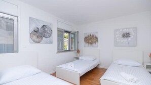 Habitación de hotel con tres camas individuales, paredes blancas y cuadros decorativos.