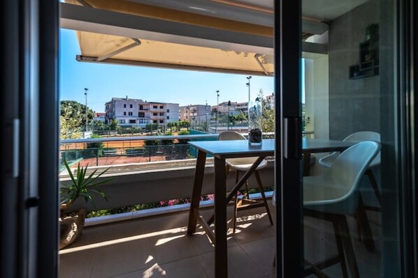 A balcony with a table and chairs, a potted plant, and a view of buildings in the background. - Classy apt W terrace@teniscourt (Split)