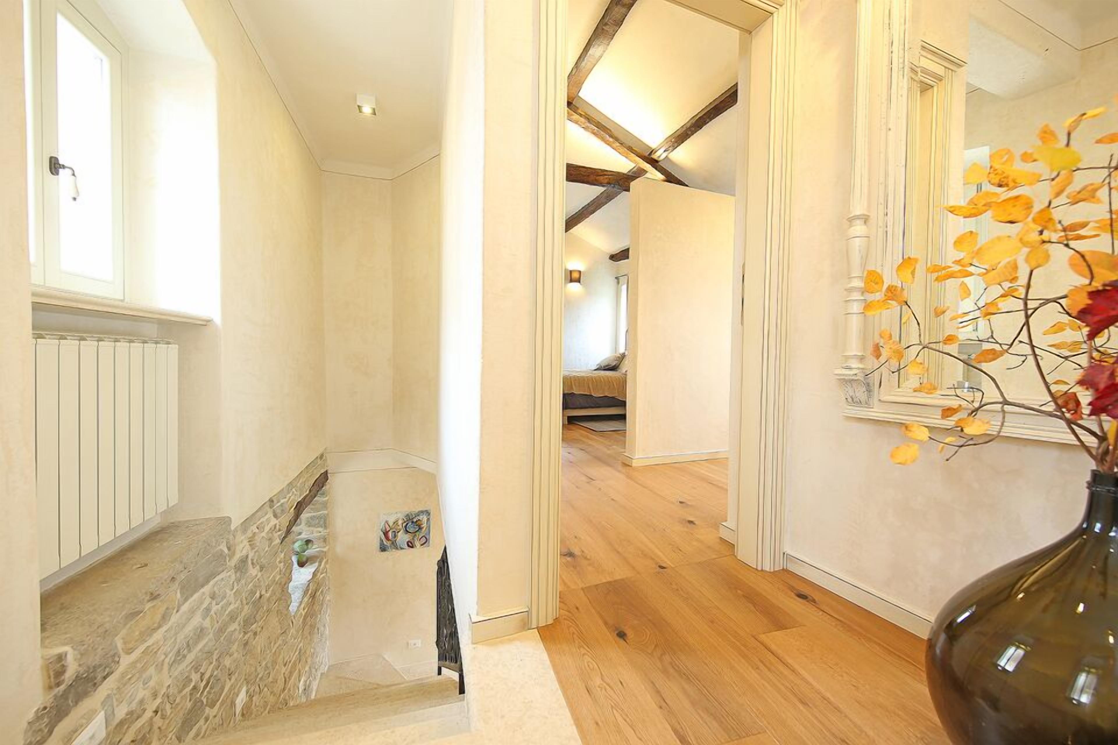 A hallway with a stone wall, wooden flooring, and a vase with autumn leaves.