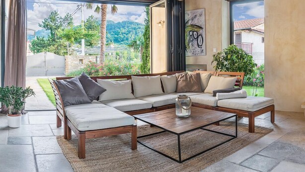 Ein modernes Wohnzimmer mit einer Eckcouch, einem Couchtisch und Blick auf einen üppigen Garten und Berge.