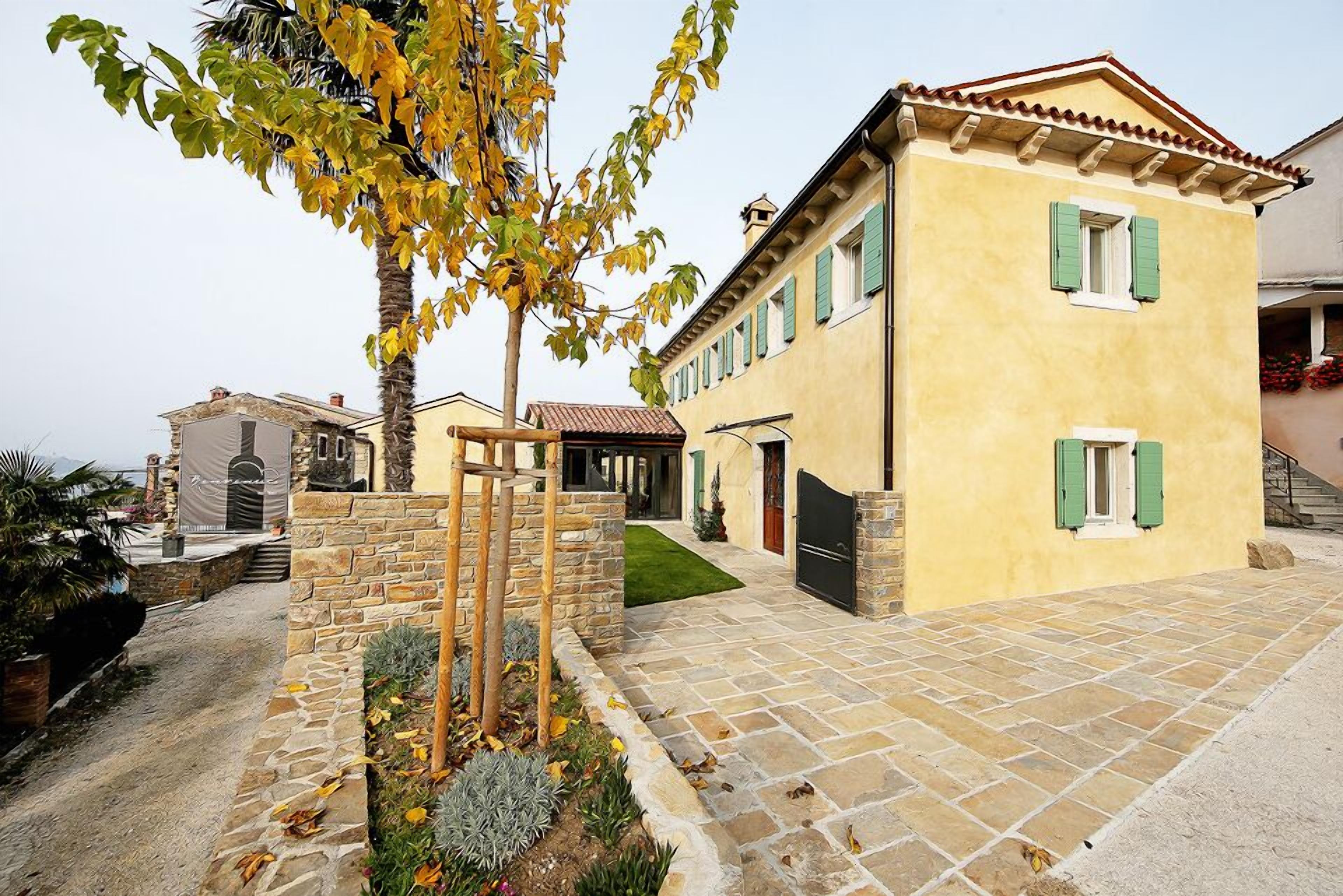 A yellow building with green shutters, a stone pathway, and a tree with yellow leaves.
