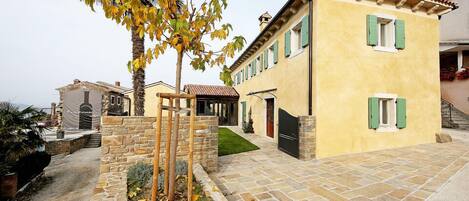 A yellow building with green shutters, a stone pathway, and a tree with yellow leaves.