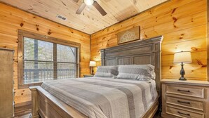 Een slaapkamer in een houten hut met een bed, nachtkastjes en een plafondventilator.