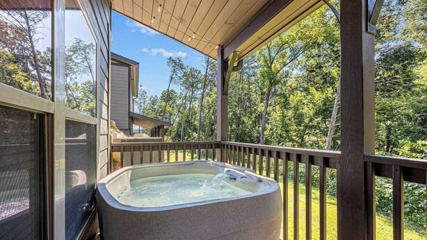 Een hottub op een houten terras, met uitzicht op bomen en een huis op de achtergrond.