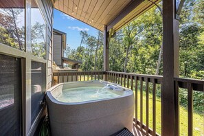 Un bain à remous sur une terrasse en bois, avec vue sur les arbres et une maison en arrière-plan.