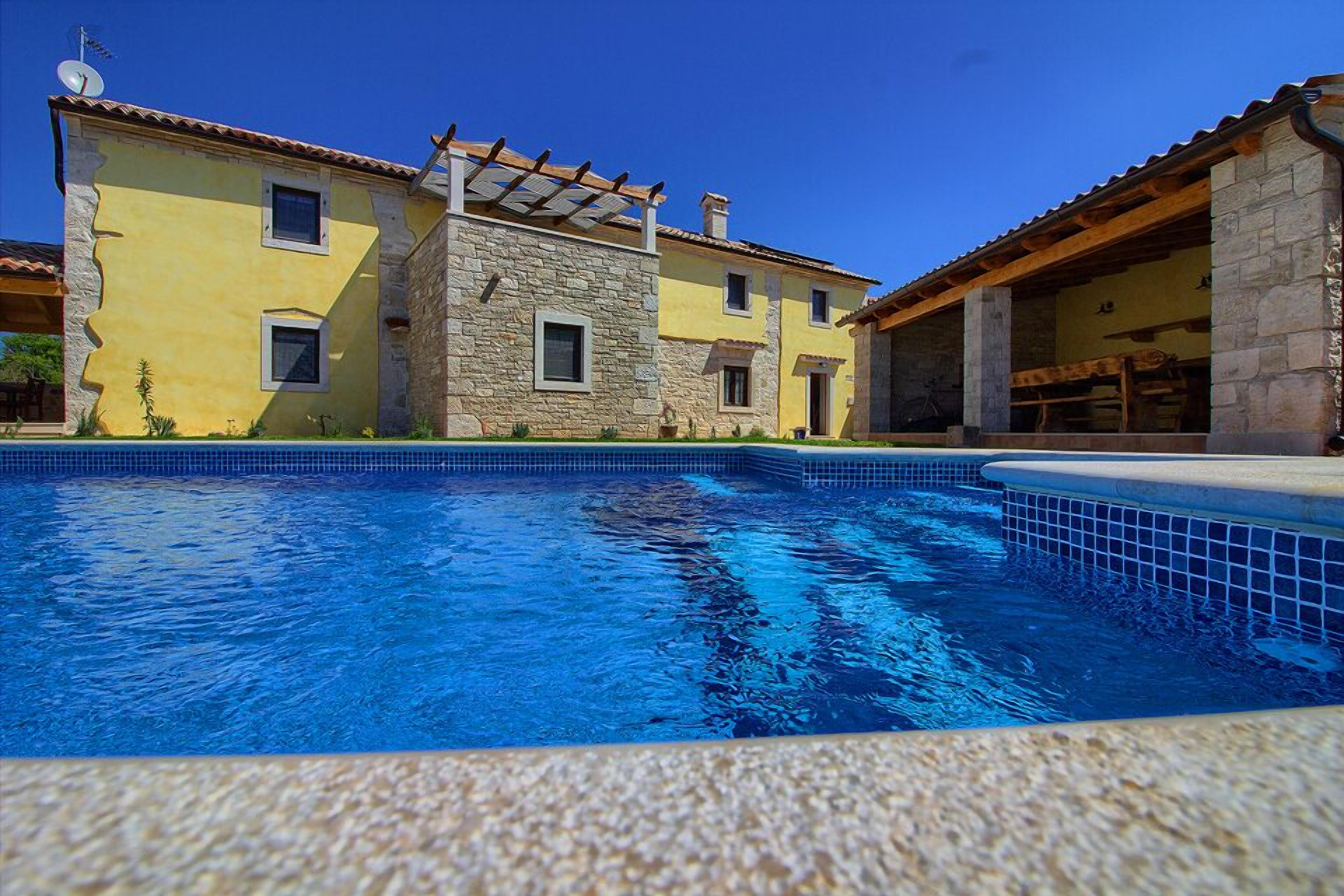 Ein Pool mit einem Gebäude im Hintergrund, dessen Fassade aus Stein ist.