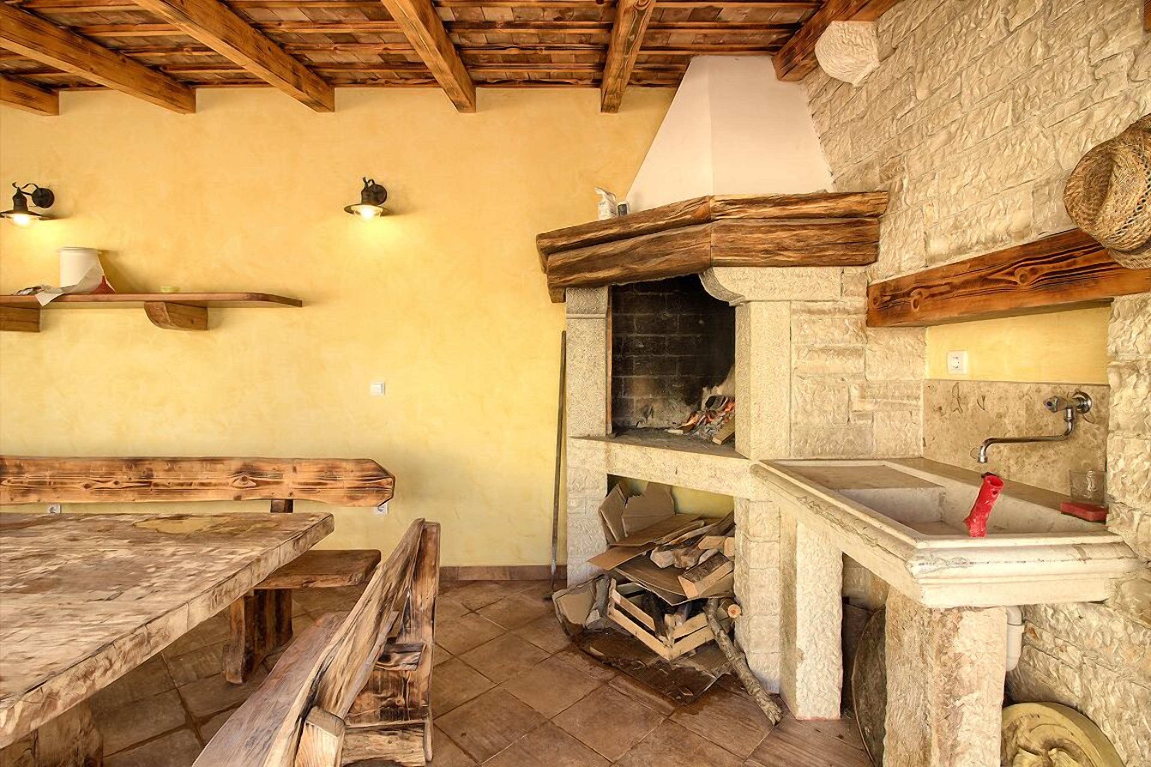 A rustic interior with a stone fireplace, wooden benches, and a stone wall.