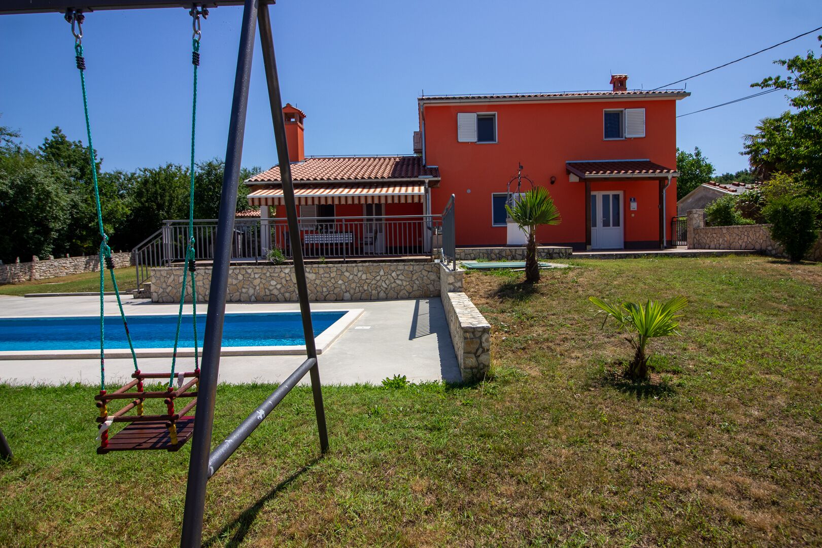 Una proprietà residenziale con piscina, altalena e muro in pietra.