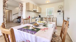 A compact kitchen with wooden cabinets, a dining table set with a floral tablecloth, and a view of the outside through a window. - Villa Marina (Istria - Paradiž) (Paradiž)