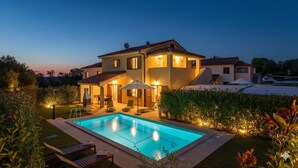 A two-story house with a swimming pool, outdoor seating, and well-lit garden areas.